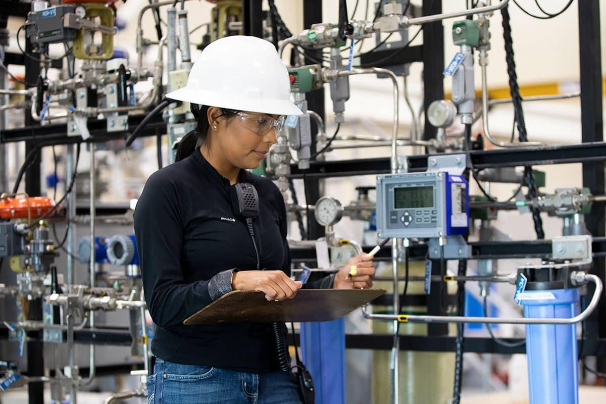 A person in a white hard hat looks at a monitor with various machines in the background